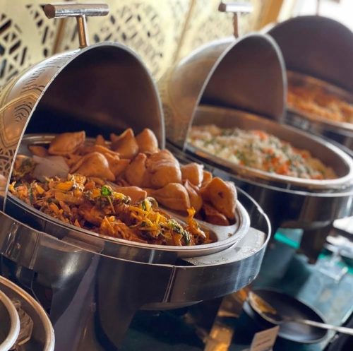 A buffet display featuring various dishes in silver chafing dishes, including rice and pastries.