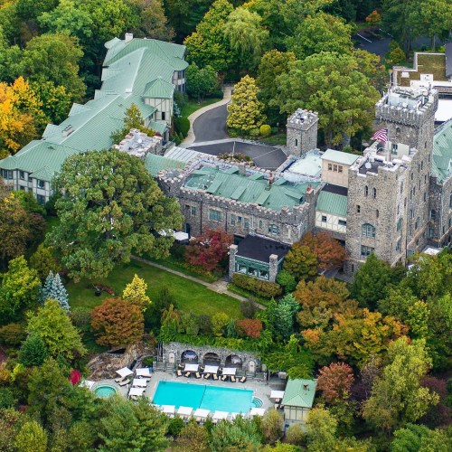 Aerial view of a lush landscape featuring a castle-like building, pool, and surrounding greenery.