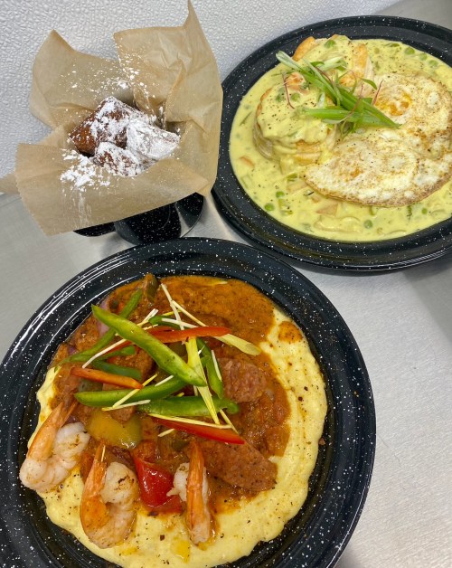 A plate of shrimp and sausage over creamy grits, with a side of eggs and a dessert of powdered sugar-dusted pastries.