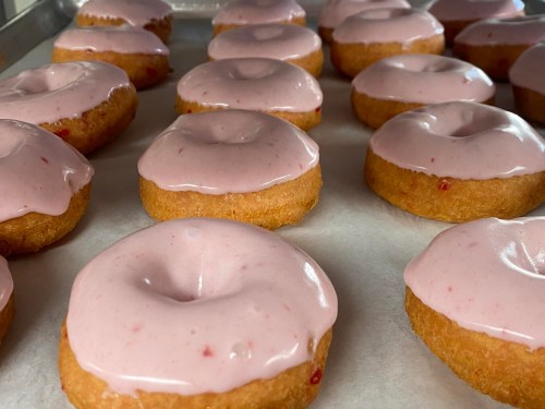 A tray of freshly baked donuts with pink frosting, arranged neatly on parchment paper.
