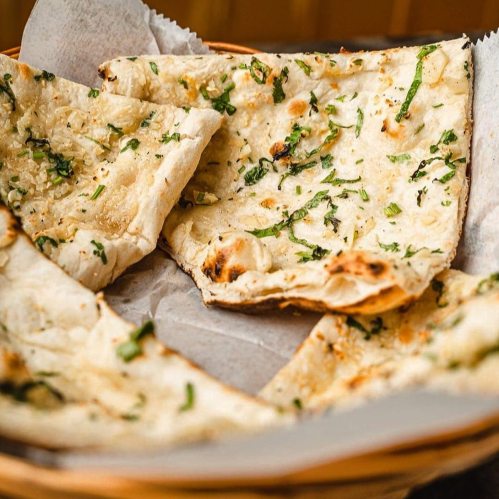 A basket of freshly baked naan bread topped with herbs and garlic.
