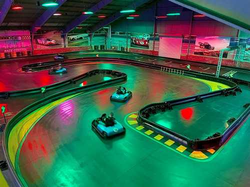 A vibrant indoor go-kart track with colorful lights and karts racing on a winding course.