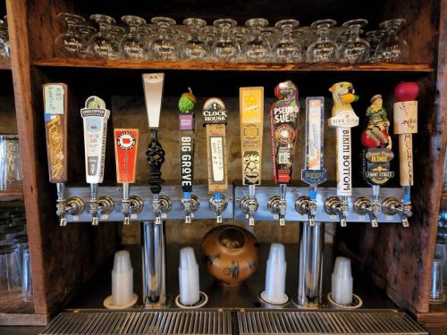 A row of colorful beer taps with various labels, set against a wooden bar backdrop.
