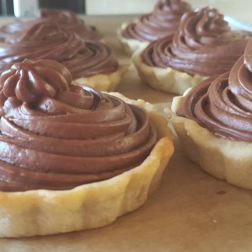Close-up of chocolate frosted tartlets on a wooden surface, showcasing swirls of rich chocolate icing.