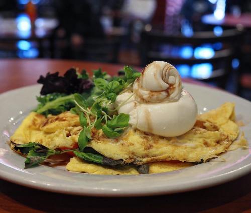 A plate of omelette topped with a poached egg and garnished with fresh greens.