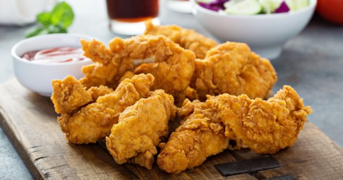 Crispy fried chicken tenders on a wooden board, served with a small bowl of dipping sauce and a side salad.
