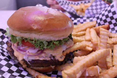 A juicy burger with lettuce, tomato, and onion, served with a side of crinkle-cut fries in a checkered basket.