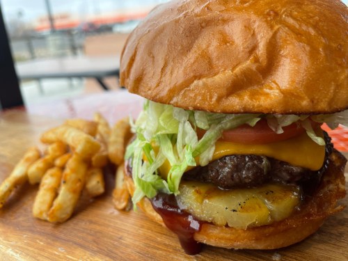 A close-up of a juicy burger with lettuce, tomato, cheese, and pineapple, served with a side of crispy fries.