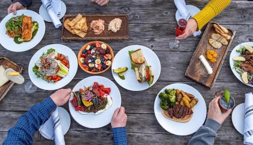 A table spread with various colorful dishes, drinks, and appetizers, enjoyed by several people.