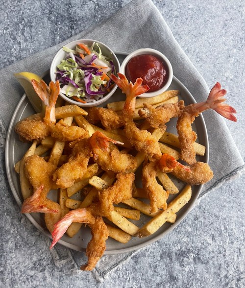 A plate of crispy fried shrimp on a bed of fries, served with coleslaw and ketchup on the side.