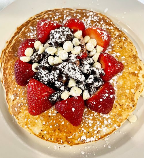 A golden pancake topped with fresh strawberries, chocolate chips, and powdered sugar.