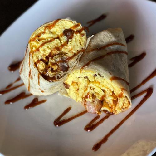 Two sliced burritos filled with scrambled eggs and meat, drizzled with sauce, on a white plate.