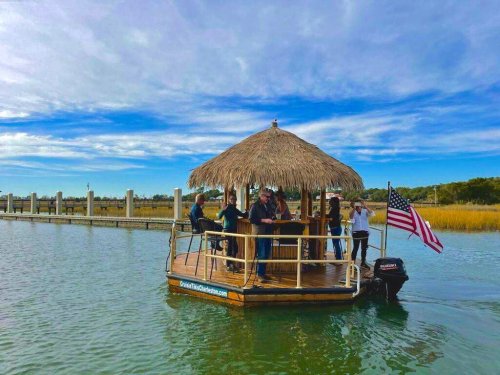 A group of people on a thatched-roof boat, enjoying a sunny day on the water, with an American flag waving.
