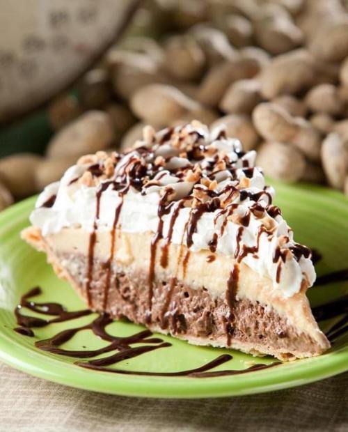 A slice of layered chocolate and peanut butter pie topped with whipped cream and chocolate drizzle on a green plate.