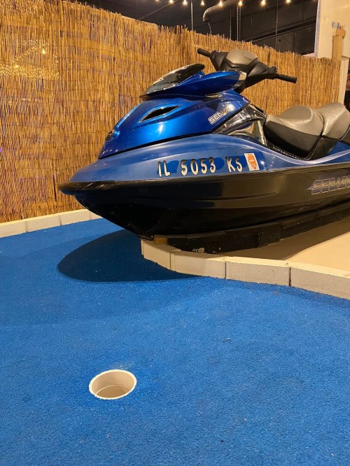A blue jet ski parked on a blue surface, with a circular hole nearby, set against a bamboo backdrop.