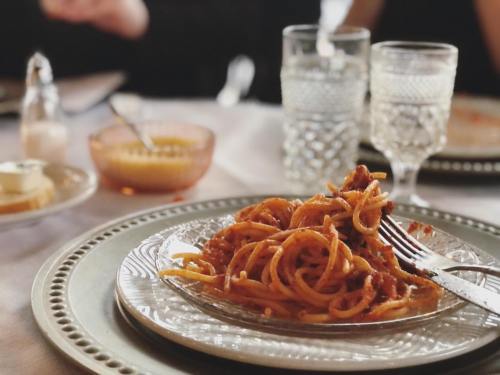 A plate of spaghetti with sauce, a fork resting on it, surrounded by glasses and small bowls on a dining table.