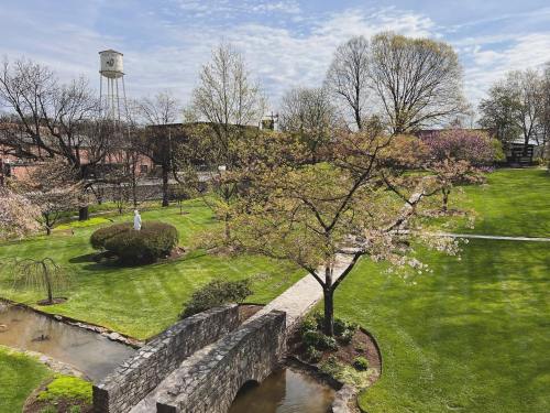 A serene park scene featuring a stone bridge, lush green grass, blooming trees, and a water tower in the background.
