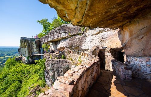 A scenic view of a rocky cliffside with a stone pathway and lush greenery, under a clear blue sky.