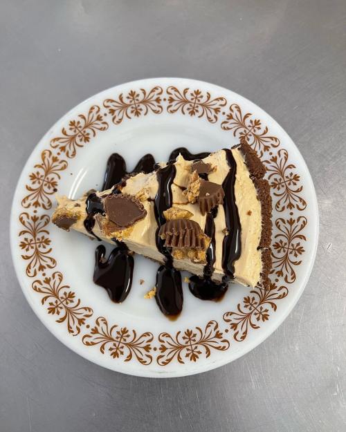 A slice of peanut butter pie topped with chocolate drizzle and peanut butter cups on a decorative plate.
