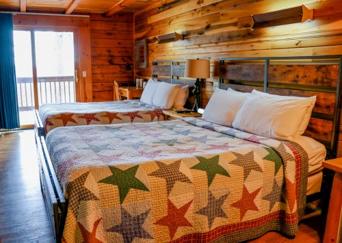 Cozy cabin interior with two beds covered in star-patterned quilts and wooden walls, featuring a balcony view.