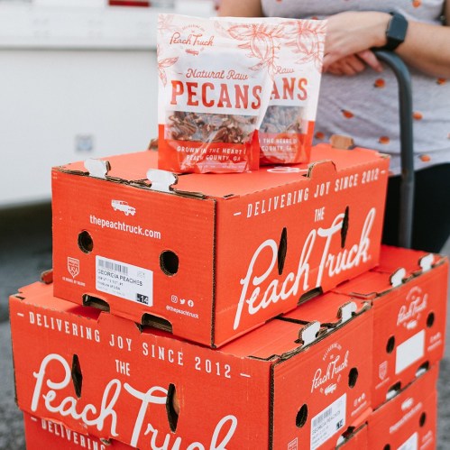 Boxes of Georgia peaches and pecans from The Peach Truck, with a person in the background holding a bag.