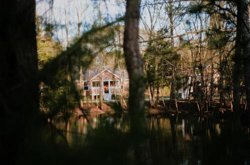 A serene view of a house by a calm lake, surrounded by trees and reflecting nature's tranquility.