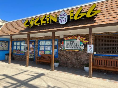 Exterior of "Chicken or the Egg" restaurant with colorful signage and benches outside, bright sunny day.