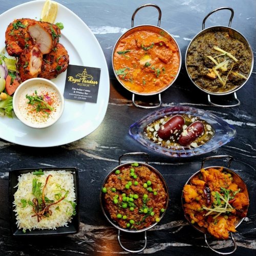 A vibrant spread of Indian dishes including grilled chicken, curries, rice, and desserts on a dark marble table.