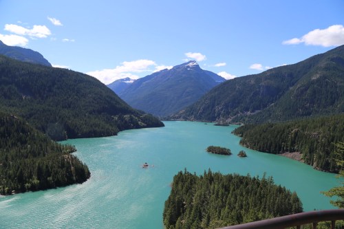 A scenic view of a turquoise lake surrounded by lush green mountains under a clear blue sky.