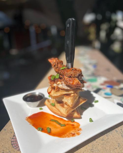 A stack of crispy waffles topped with chicken, drizzled with sauce, and garnished with green onions on a white plate.