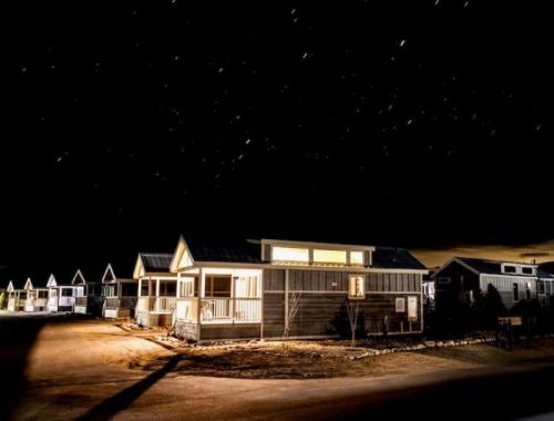 A quiet neighborhood of houses illuminated at night, with a starry sky above and a dark road in the foreground.