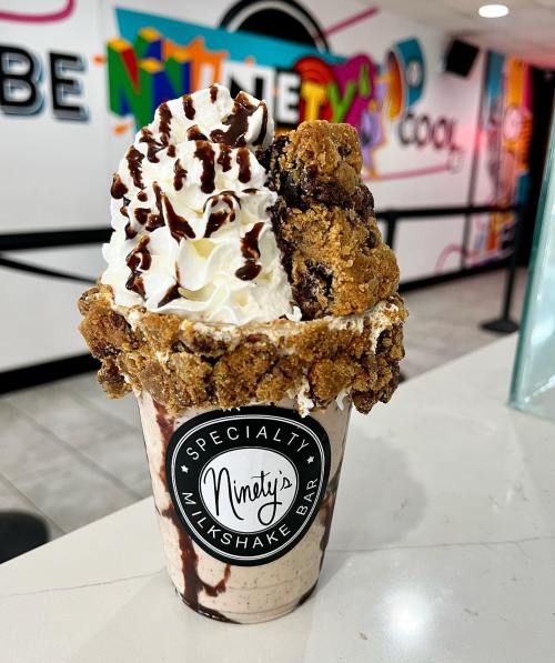 A decadent milkshake topped with whipped cream, chocolate drizzle, and a cookie crust, served in a branded cup.
