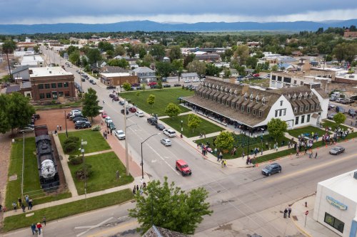 Aerial view of a small town with a historic building, green space, and people gathered outside, surrounded by mountains.