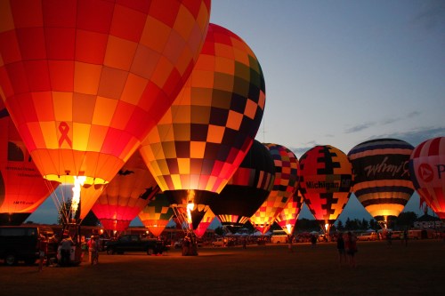Colorful hot air balloons illuminated at dusk, creating a vibrant display against the evening sky.