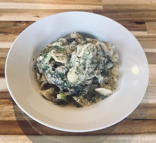 A bowl of pasta topped with creamy sauce and herbs, served on a wooden table.