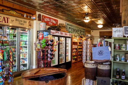 A cozy store interior featuring shelves of snacks, drinks, and rustic decor, with a wooden barrel in the foreground.