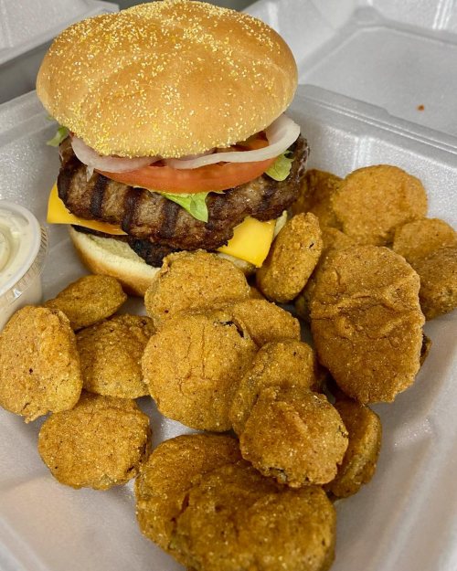 A hamburger with lettuce, tomato, and cheese, served with a side of golden chicken nuggets in a takeout container.