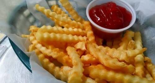 A serving of crinkle-cut fries with a small cup of ketchup on a tray.