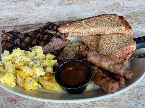 A hearty breakfast plate with grilled steak, scrambled eggs, hash browns, sausage links, and toasted bread.