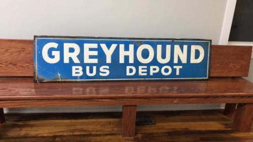 Vintage Greyhound Bus Depot sign displayed on a wooden bench in a simple interior setting.