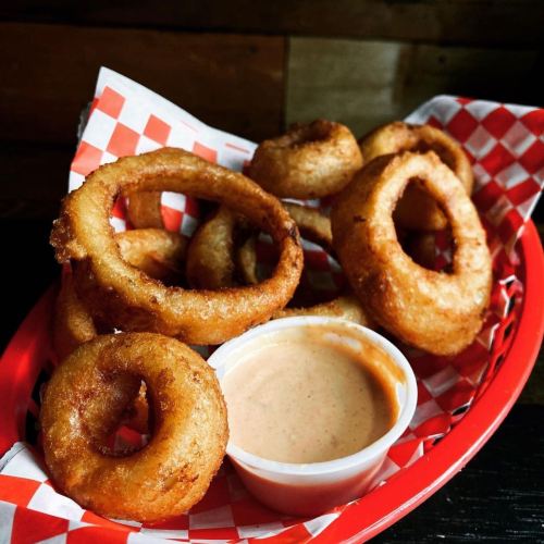 A red basket filled with golden-brown onion rings and a small cup of dipping sauce.