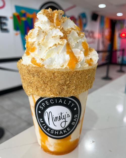 A delicious milkshake topped with whipped cream and crushed cookies, served in a decorative cup at Ninety's Milkshake Bar.