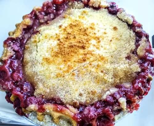 A freshly baked cherry pie with a golden-brown crumb topping and a rich, red filling.
