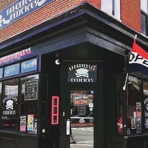 Exterior of a restaurant named "Dangerously Delicious," featuring a black facade and colorful signage.