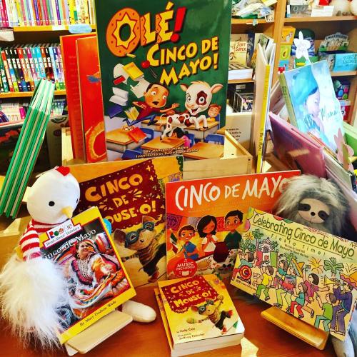 A colorful display of children's books about Cinco de Mayo, featuring plush toys and festive decorations.