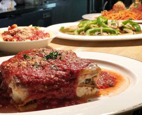 A plate of lasagna topped with marinara sauce and herbs, with pasta and vegetables in the background.