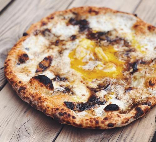 A close-up of a pizza with a golden yolk in the center, topped with melted cheese and charred edges, on a wooden surface.