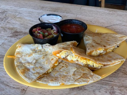 A yellow plate with quesadillas filled with cheese and chicken, served with salsa and sour cream on the side.