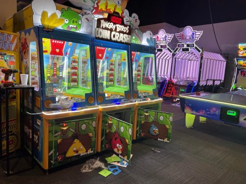 Three "Angry Birds Coin Crash" arcade machines with colorful graphics, surrounded by other arcade games in a dimly lit room.
