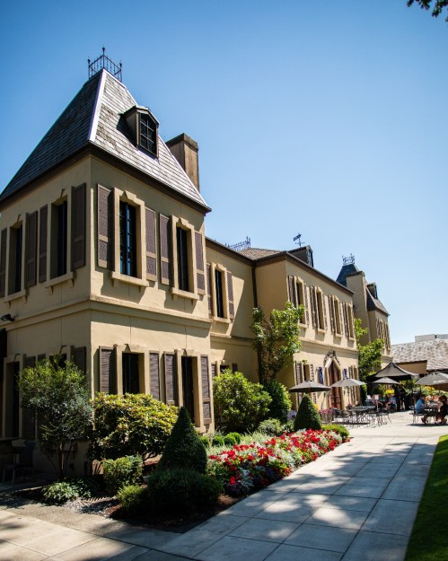 A charming building with a steep roof, surrounded by colorful flowers and greenery under a clear blue sky.
